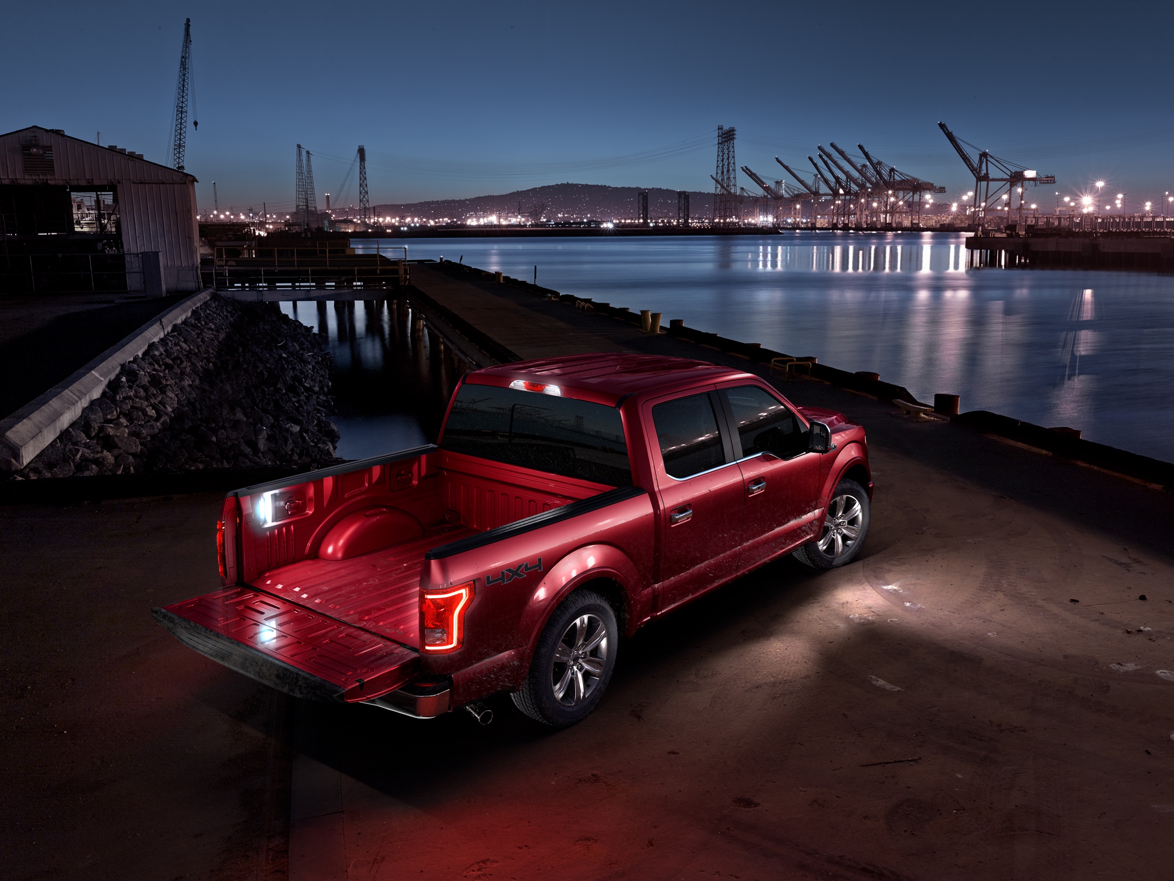 Red Ford F-150 illuminated at night beside an industrial harbor