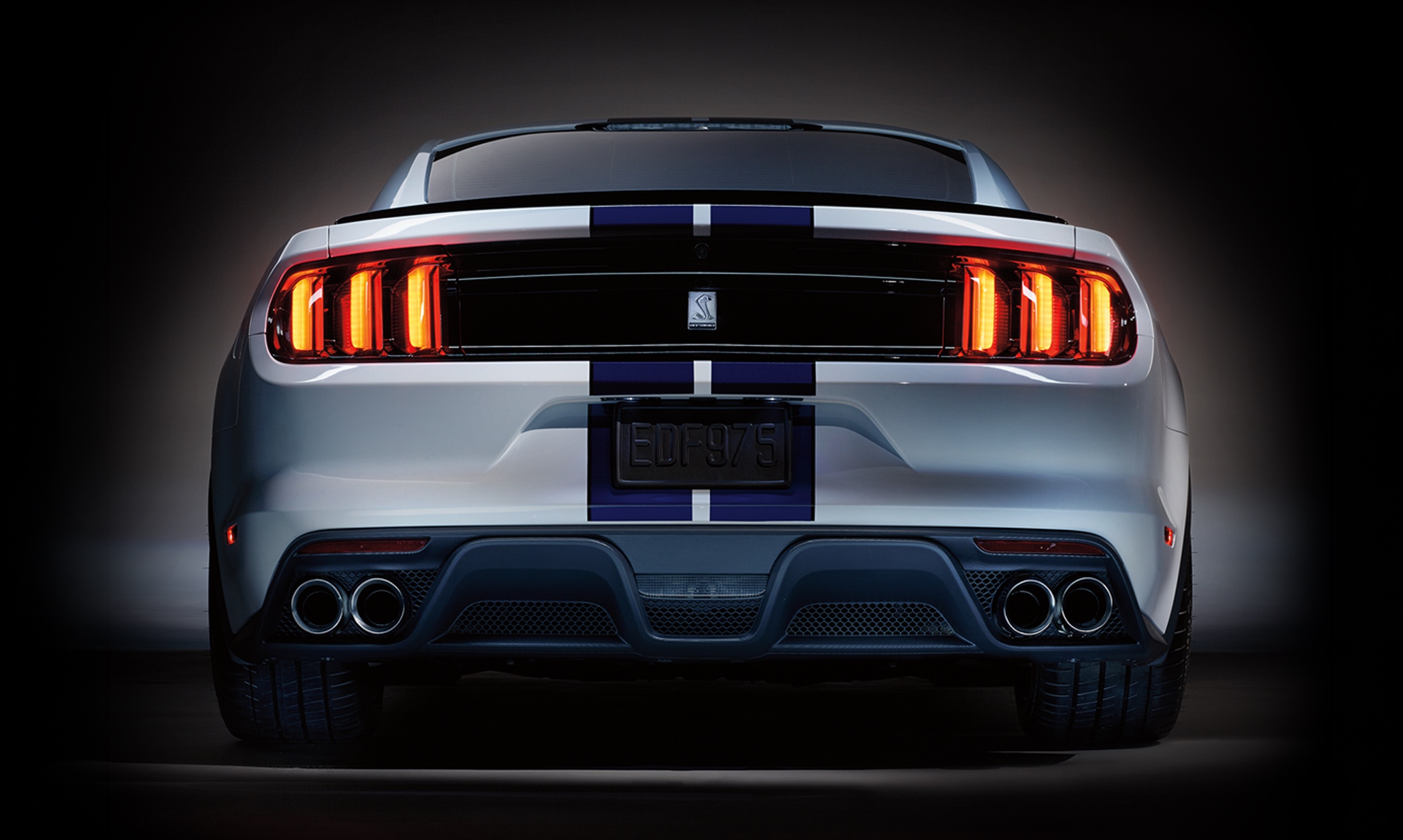 Rear studio view of a white Mustang Shelby GT350 with illuminated tri-bar taillights