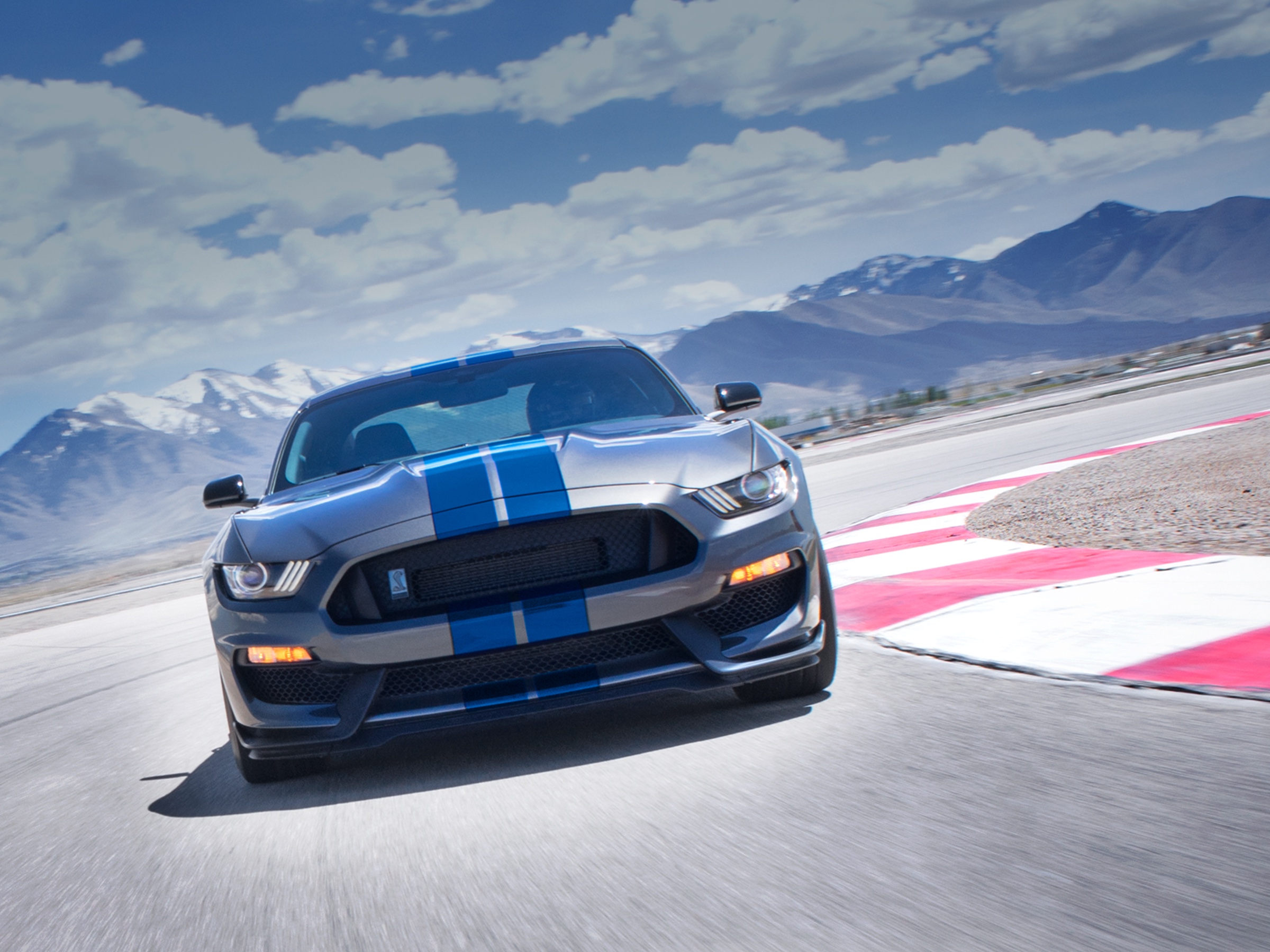 Gray Mustang Shelby GT350 cornering on a racetrack beneath a mountain landscape