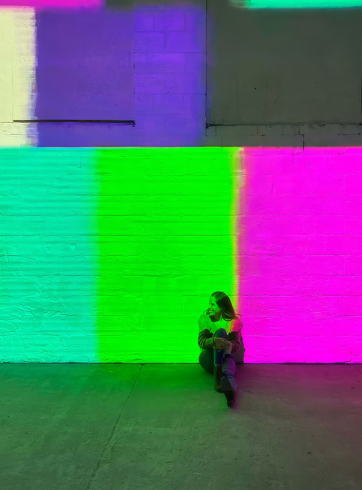 Visitor seated beneath large fields of green, violet, and magenta projected light