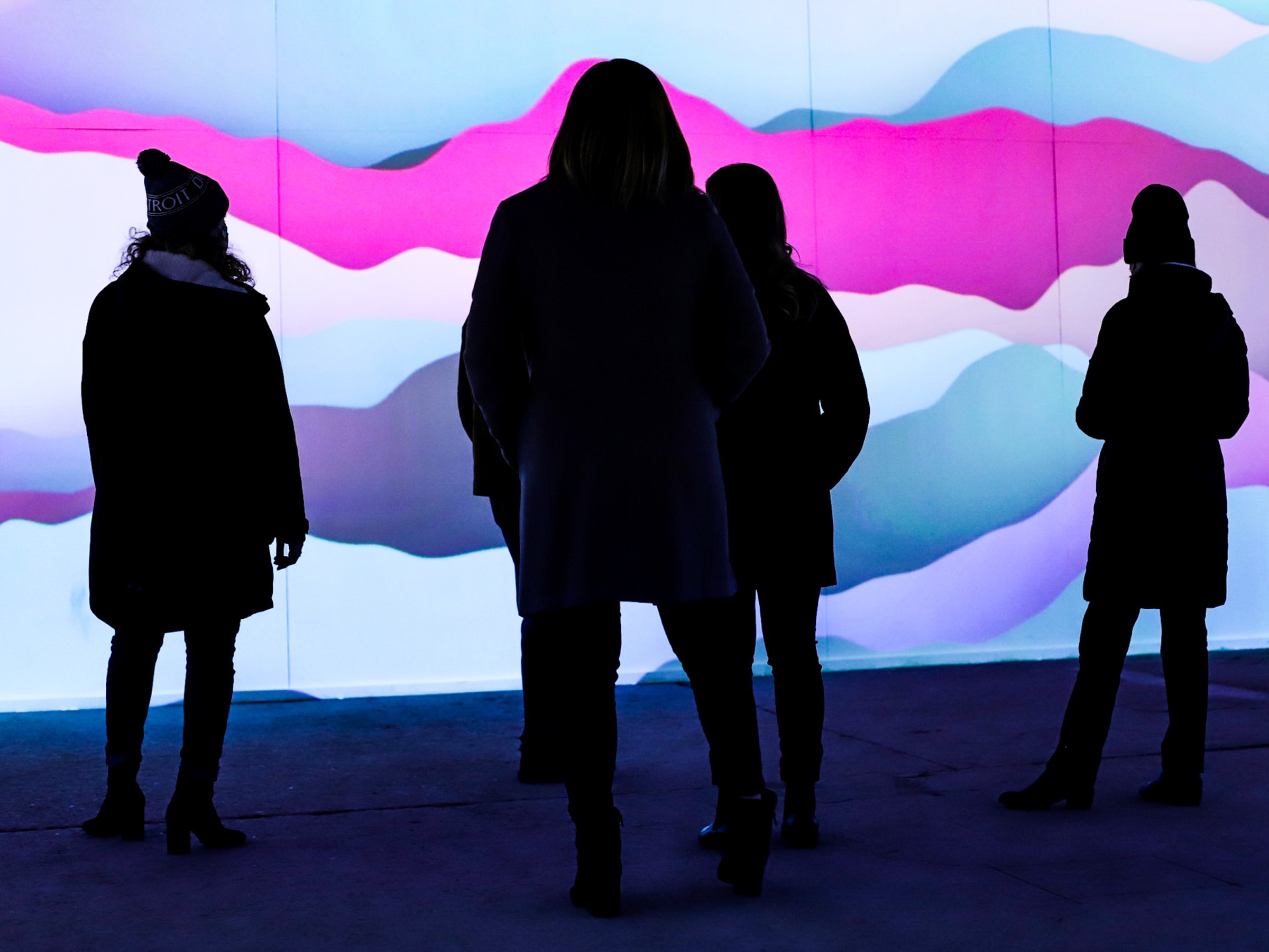 Visitors silhouetted against blue, pink, and violet wave-like projections inside Spacecraft