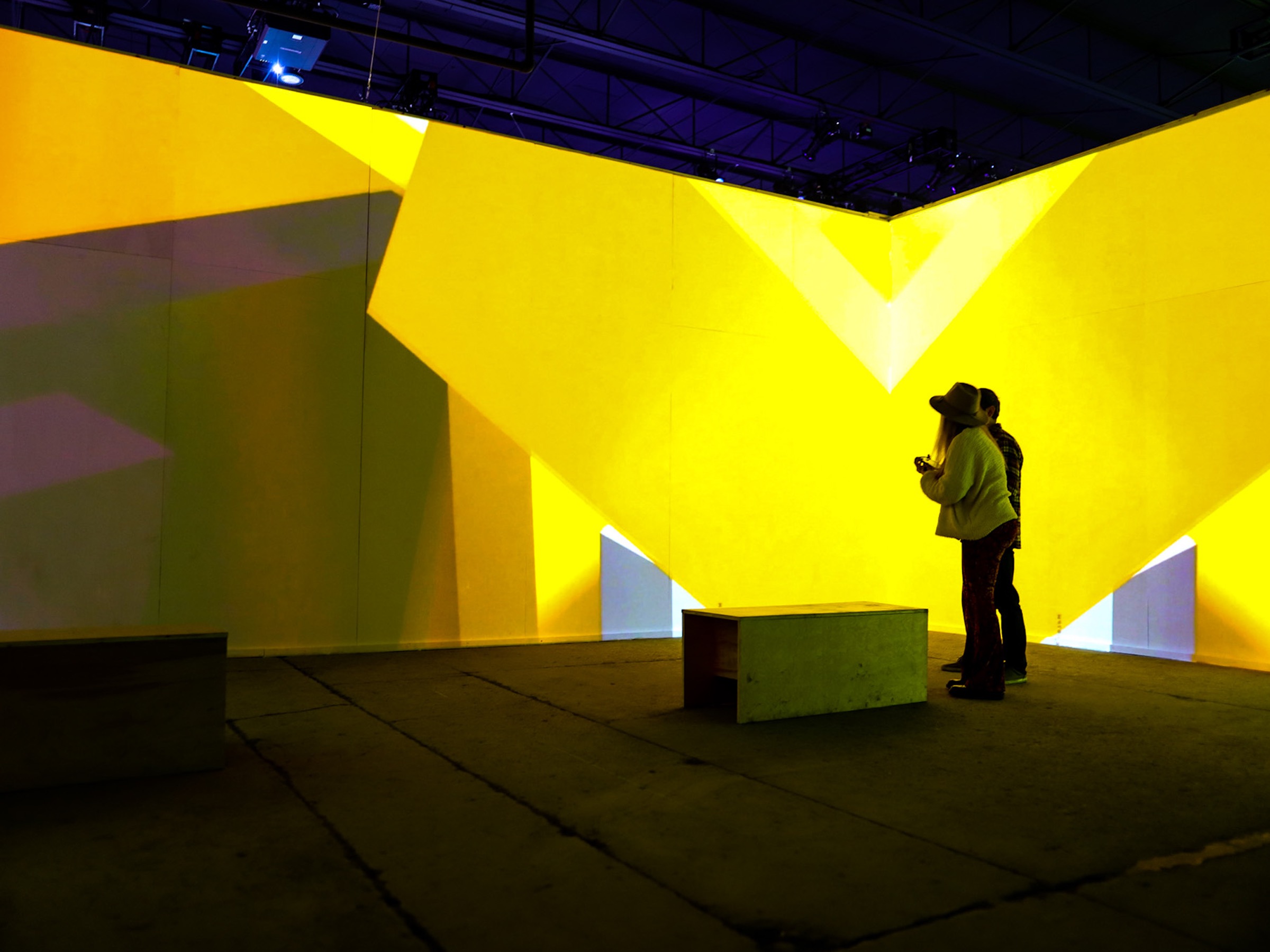 Visitors standing inside a yellow geometric light projection at Spacecraft